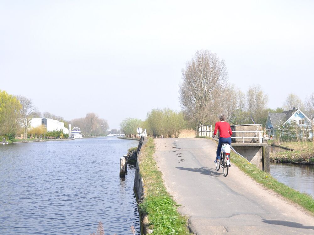 Fietspad tussen twee waterpartijen in recreatiegebied Vlietland bij Leidschendam met een fietser en groene oevers